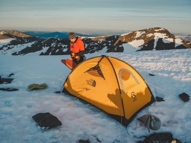 En person invid ett tält på en snöig bergsplätt