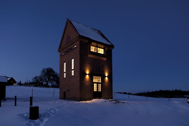 Transformatortornet, en hög tegelbyggnad, om natten. Det lyser varmt ur fönstren.