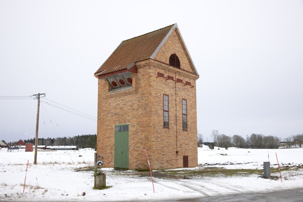 Tonet i Veckelstad: En hög tegelyggnad med sluttande tak och grön ytterdörr