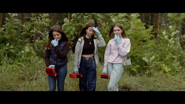 Tre unga personer med bärplockarutrustning i en skog