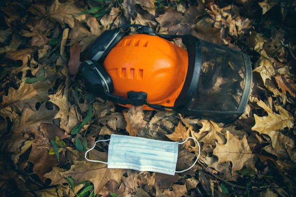 En bygghjälm som ligger bland löv på marken, invid ett engångsmunskydd.