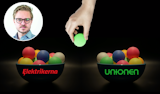 En hand som håller en grön boll över två skålar fulla med färgglada bollar. På en ena skålen står det Elektrikerna, på den andra Unionen. En bild på Anton Levein är monterad i hörnet.