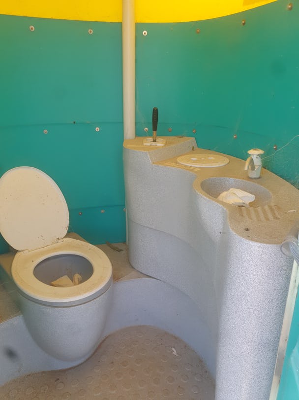 En lortig toalett i ett rum med turkosa väggar.