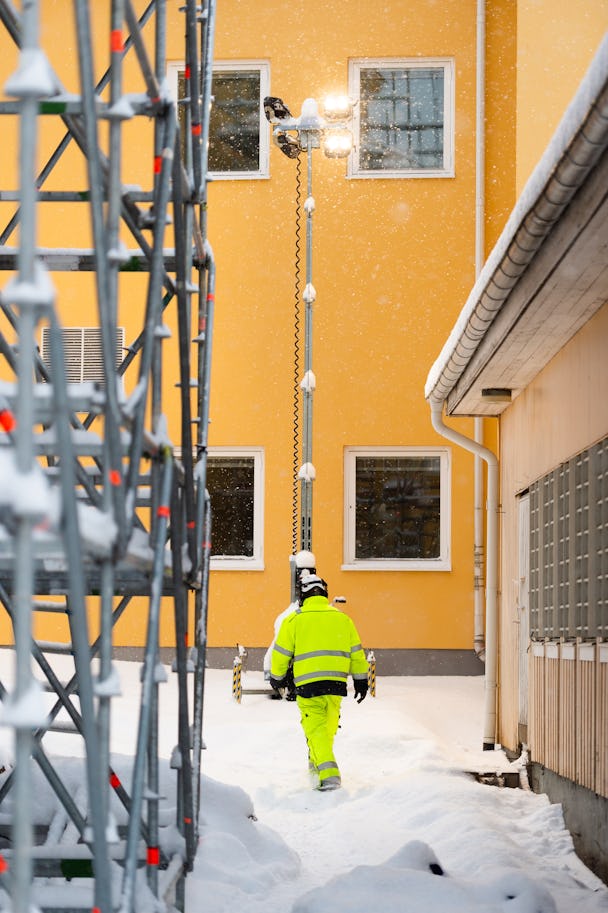 En person i arbetskläder rör sig utomhus i snön på bygget