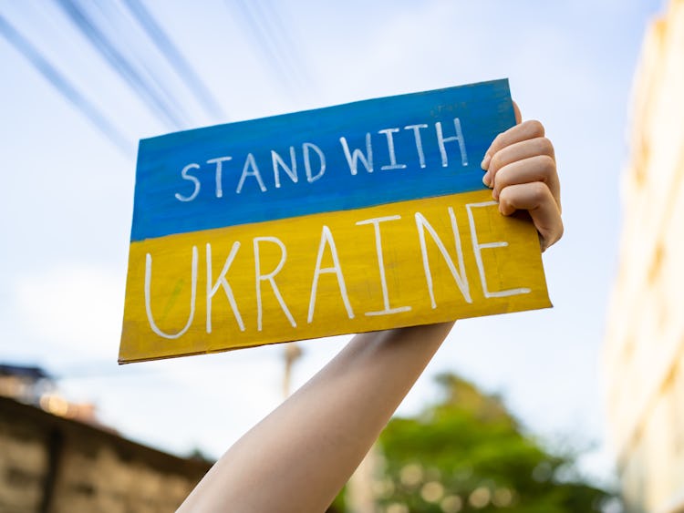 En hand håller upp en skylt med Ukrainas flagga, samt texten: "Stand with Ukraine."