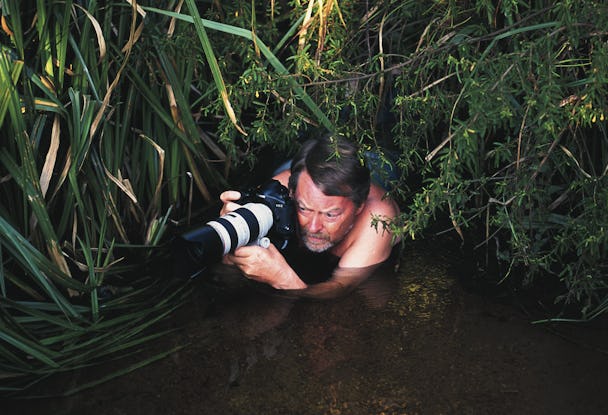 Dick Persson krälar genom vatten med en kamera med stort objektiv.
