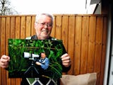 Dick Persson håller upp ett foto på sig själv med en kamera med stort objektiv.
