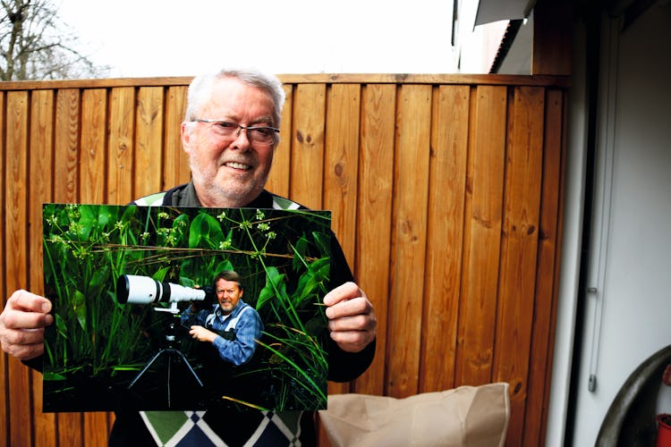 Dick Persson håller upp ett foto på sig själv med en kamera med stort objektiv.