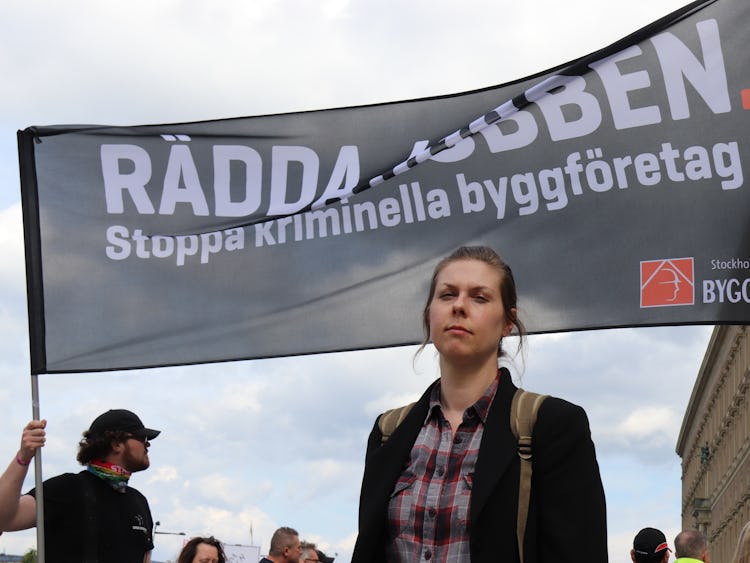 Karolina Dahl framför en banderoll där det står: "Rädda jobben. Stoppa kriminella byggföretag."