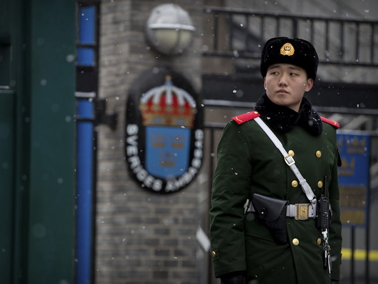 En militär står på vakt, svenska ambassadens logga syns suddigt i bakgrunden.