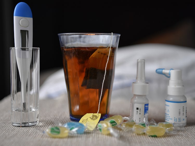 Febertermometer, ett glas te, mediciner och halstabletter.