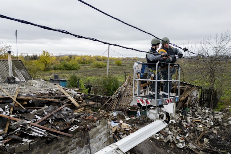 Två elektriker i en skylift lagar en ledning, i ett krigshärjat Ukraina.