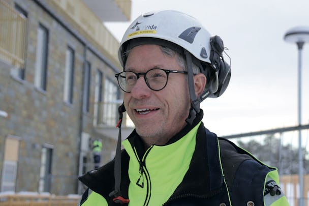 Michael Norberg som bär hjälm och glasögon framför en byggnad.