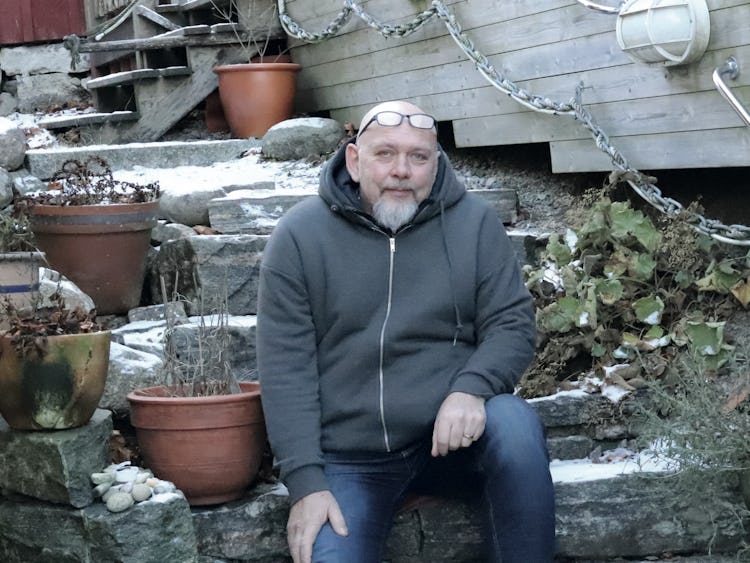 Henric Andersson som sitter på trappan till ett hus med krukväxter.
