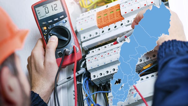 En man använder en multimeter på en elektrisk panel och en karta över Sverige.