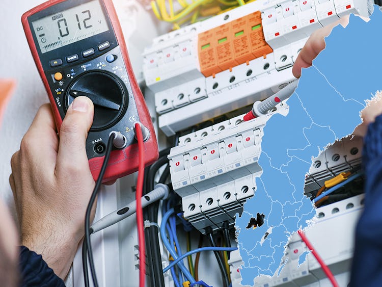 En man använder en multimeter på en elektrisk panel och en karta över Sverige.
