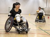 Kvinna i rullstol håller en boll och spelar rullstolsrugby.