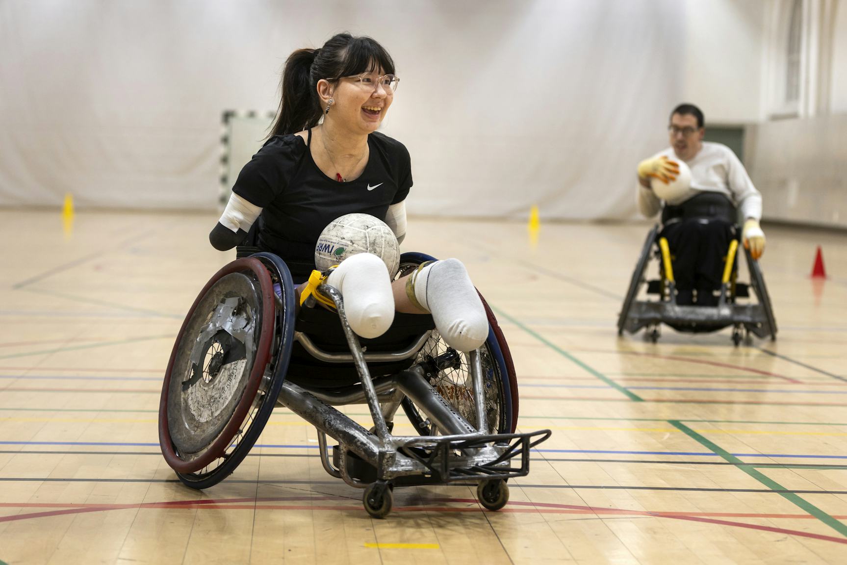 Kvinna i rullstol håller en boll och spelar rullstolsrugby.