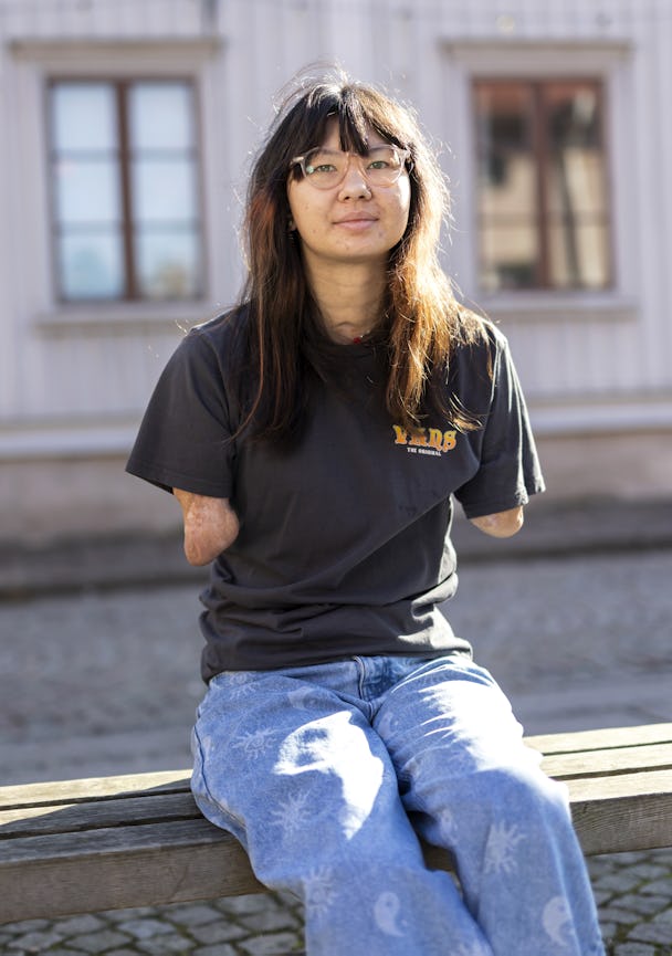 En kvinna i glasögon och svart t-shirt sitter på en träbänk.