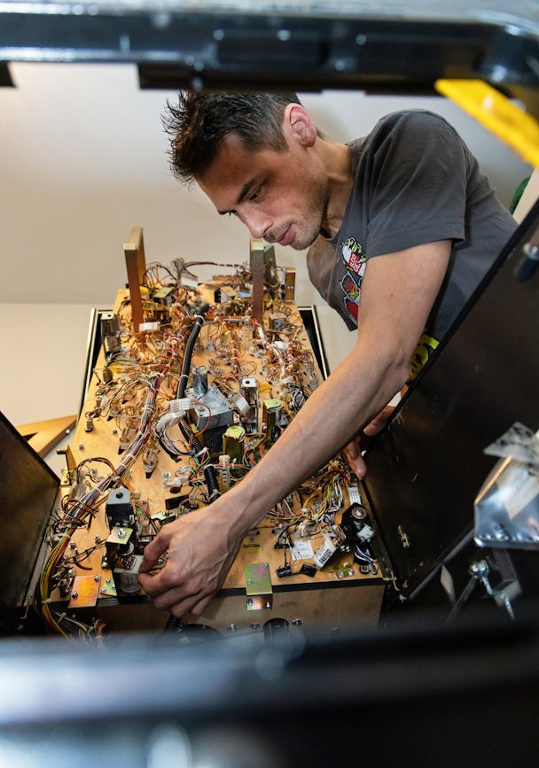 En person i en grå t-shirt arbetar med komplexa kablar och komponenter inuti en öppen elektronisk enhet.