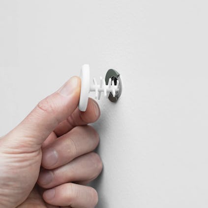 En hand trycker in en vit väggplugg i ett hål på en vit vägg.
