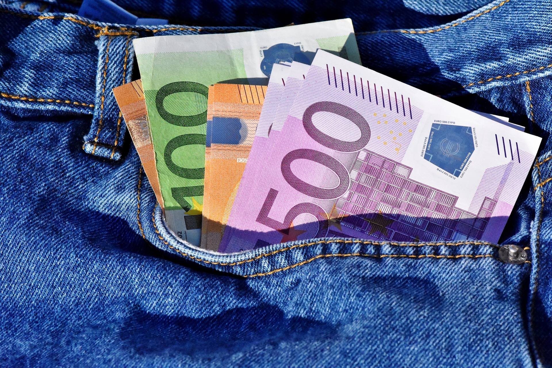 Bilden är en närbild på sidofickan på ett par blå jeans. Sju olika Euro-sedlar sticker upp ur fickan.