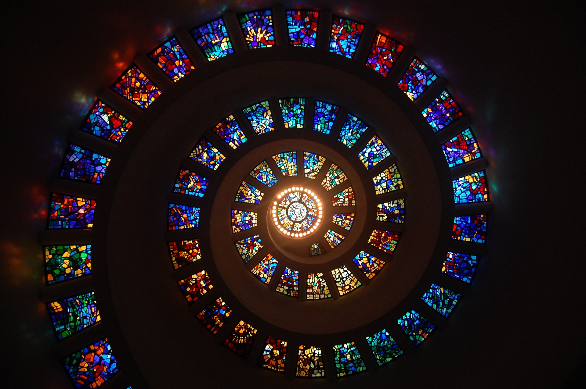 Bilden föreställer en spiral bestående av dussintals förgglada moasaikfönster som ringlar upp längs ett kupolformat tak. I mitten är ett runt fönster som släpper in starkt ljus.