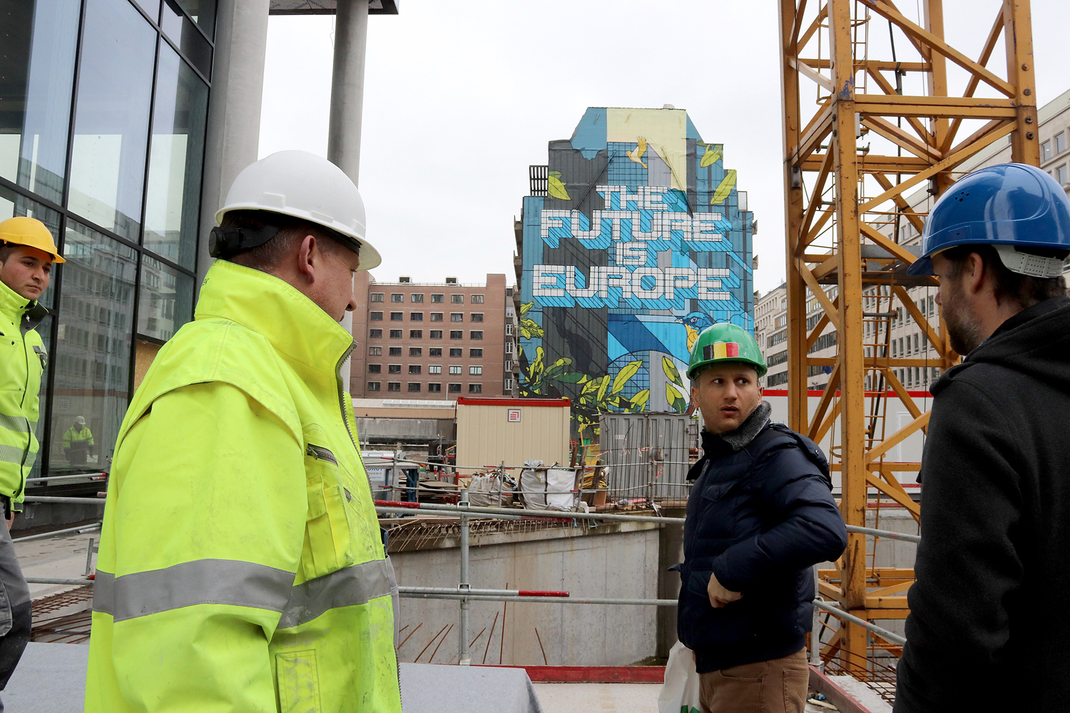 Bilden föreställer fyra byggnadsarbetare på en byggarbetsplats i Bryssel. I bakgrunden ser man en byggnad med texten The Future Is Europe på.
