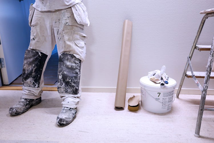 Benen och fötterna på en målare som står vid en vägg med sina verktyg