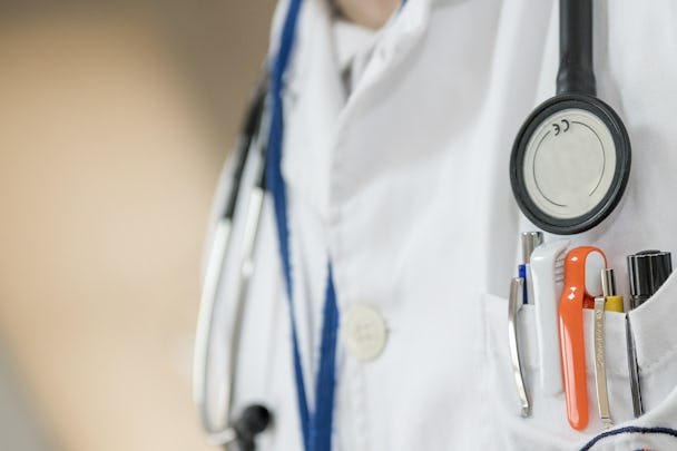En person i läkarrock, med ett stetoskop runt halsen och pennor i bröstfickan.