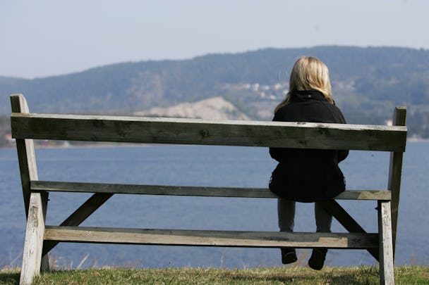 En person sitter ensam längst ut på en bänk som är vänd mot en sjö.