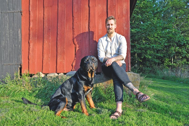 Jakob Nilsson sitter vid en röd husknut med en hund bredvid sig.