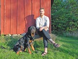 Jakob Nilsson sitter vid en röd husknut med en hund bredvid sig.