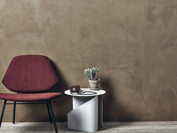 Ett rum med en vägg målad med spackelfärg. Framför väggen står en stol och ett bord med en växt på.