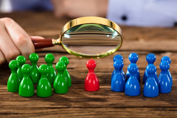 En person betraktar spelpjäser genom ett förstoringsglas. Det finns två grupper av pjäser, en grön och en blå. En ensam röd pjäs står i mitten.