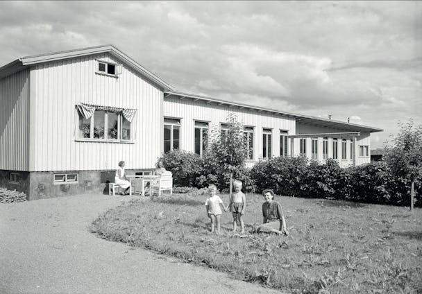 En svartvit bild på Petterslund från när det var nybyggt 1940. Några barn och vuxna står och sitter på gräsmattan.