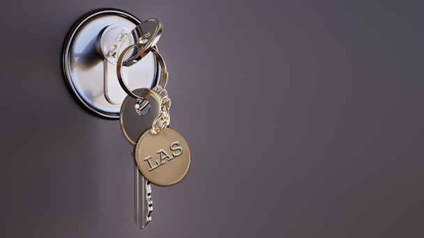 En nyckelknippa i ett dörrlås. På nyckelbrickan står det "LAS"