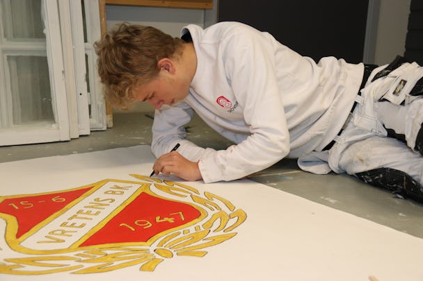 Kimi Nurminen målar en vapensköld på golvet.