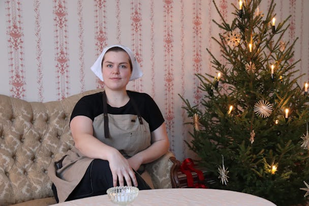 Johanna i bagerikläder framför en tapetserad vägg och en julgran.
