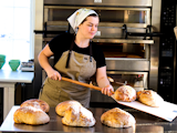 Johanna i bagerikläder arbetar med bröd på en brödspade.