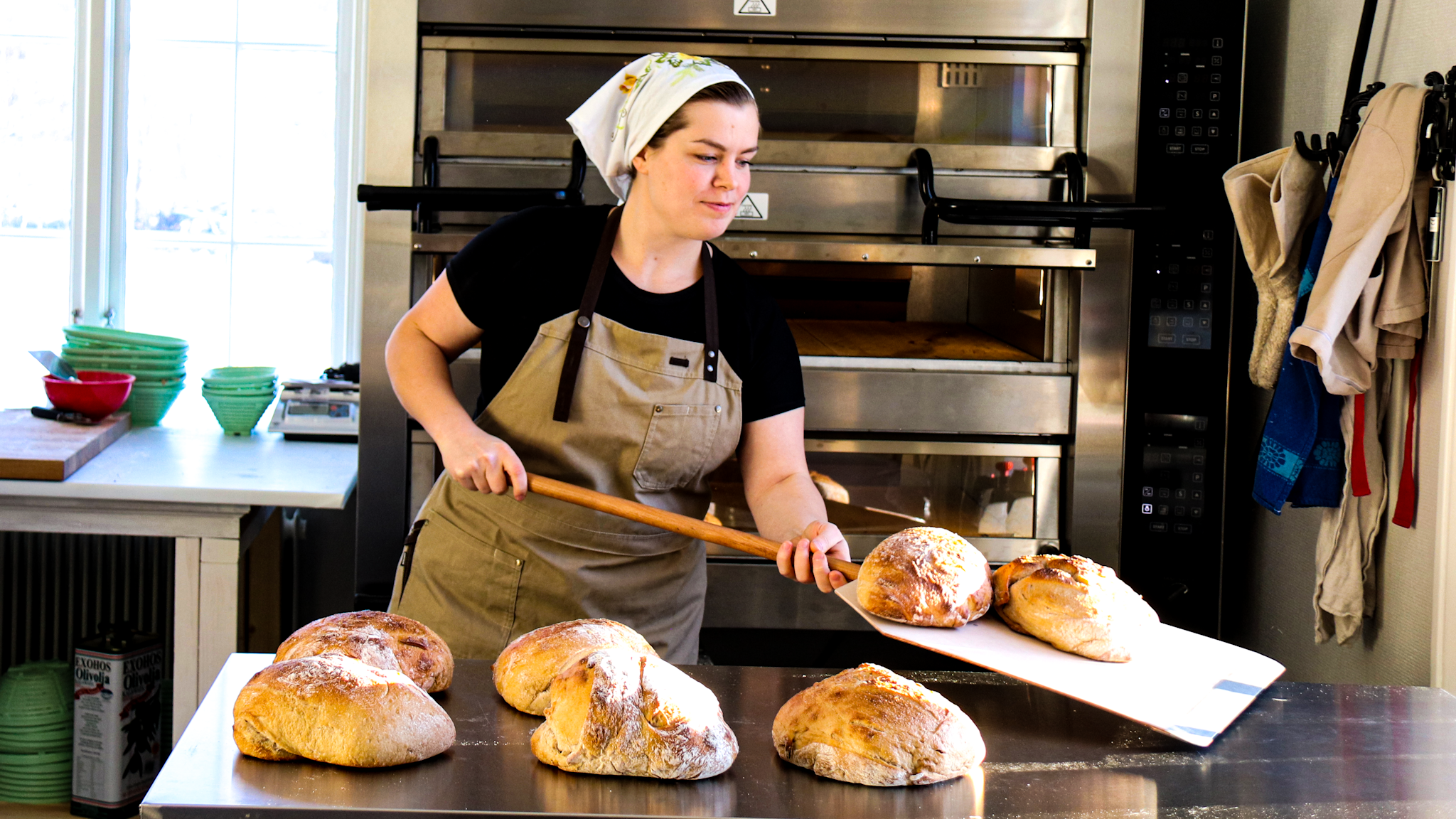Johanna i bagerikläder arbetar med bröd på en brödspade.