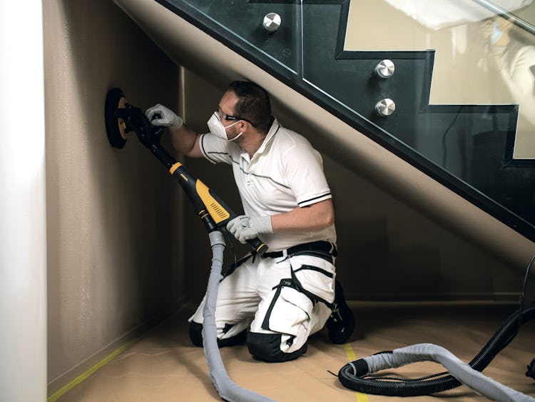 En person arbetar med slipen under en trappa