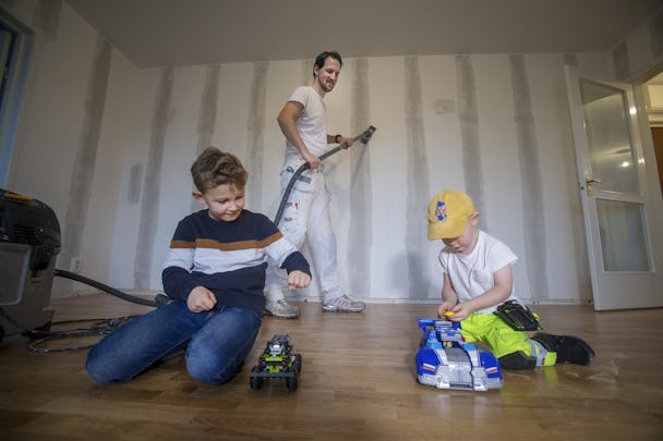 Johan dammsuger en vägg medan två barn leker på golvet.