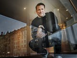 Tobias Baudin sitter vid ett fönster som speglar byggnader i centrala Stockholm