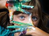 Ett barn med målarfärg på händerna håller upp fingrarna som en ram kring sitt ena öga