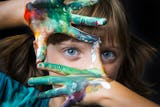 Ett barn med målarfärg på händerna håller upp fingrarna som en ram kring sitt ena öga