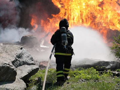 Ryggtavlan på en brandman som sprutar vatten mot en stor eldsvåda.