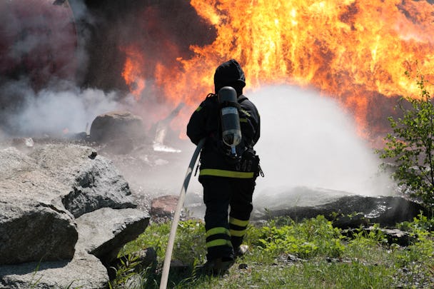 Ryggtavlan på en brandman som sprutar vatten mot en stor eldsvåda.