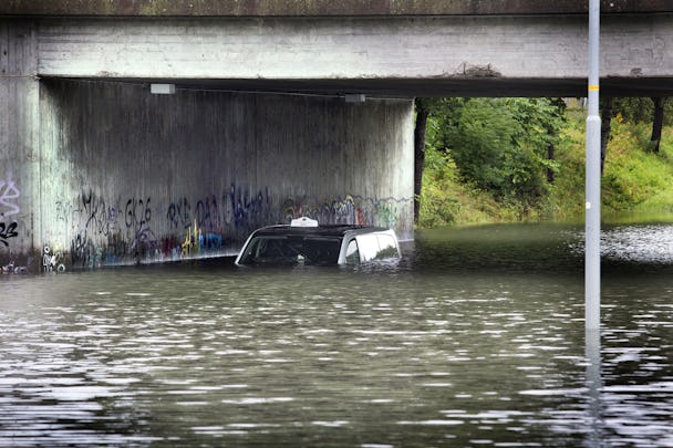 Översvämning. Under en viadukt står en bil, men bara taket sticker upp över vattenytan.