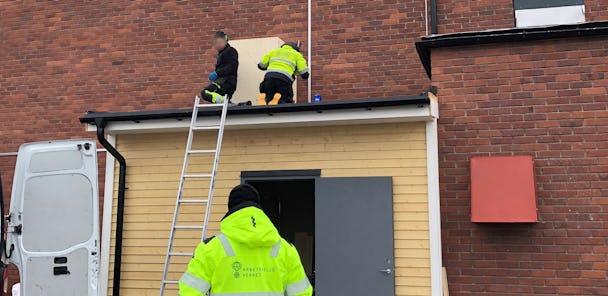 Några personer kontrollerar ett tak med hjälp av en stege.